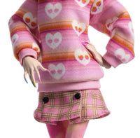 Monster High x Wednesday Enid Sinclair Doll close-up of her outfit - pink fashion aesthetic including a poink and orage striped turtleneck with heart shaped skulls, a plaid skirt, and marbled tights.