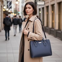 Woman in a beige coat holding a navy blue handbag on a city street.