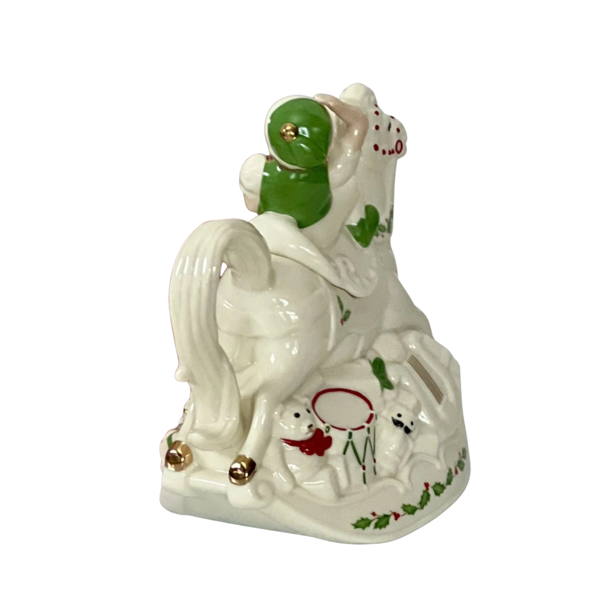 Lenox cream colored hand-painted porcelain holiday teapot with a smiling elf in a green hat on a rocking horse with a teddy bear in a red bow, a drum and a nutcracker with a black mustache at the base on top of a green holly design on a white background. 